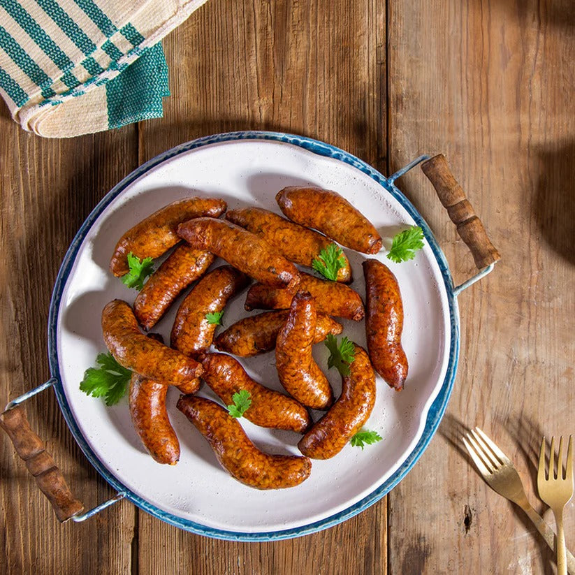 A plate of Mombar, garnished with parsley, rests on a wooden table beside two gold forks and a green-striped towel. Natural light highlights the delicious, rustic appeal of this traditional beef tripe dish.