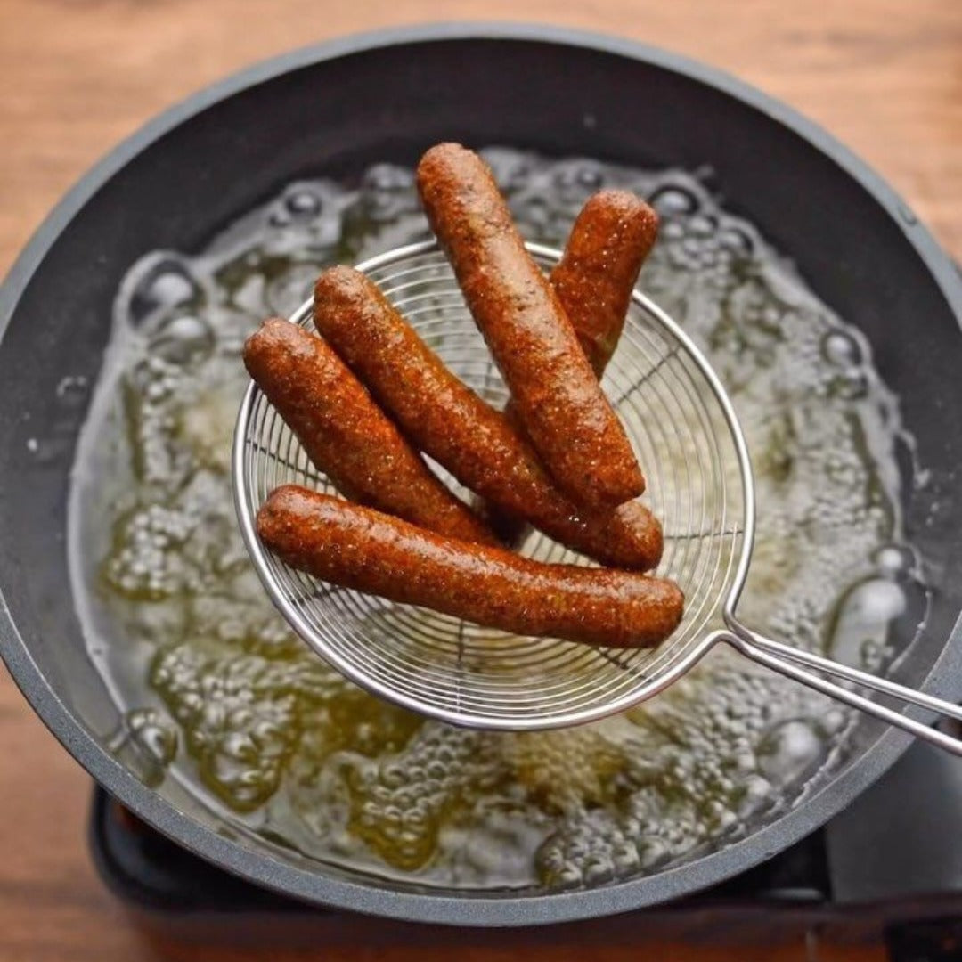 A skimmer holds several fried, brown Kufta rice snacks over a pan of hot bubbling oil, suggesting they have just been deep-fried.