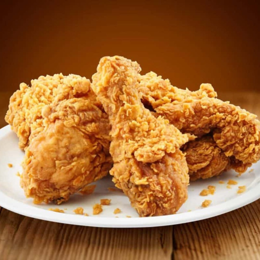 A plate of Fried Chicken with crispy, golden brown drumsticks and thighs rests on a wooden surface against a warm brown background.