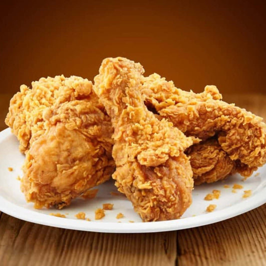 A plate of Fried Chicken with crispy, golden brown drumsticks and thighs rests on a wooden surface against a warm brown background.