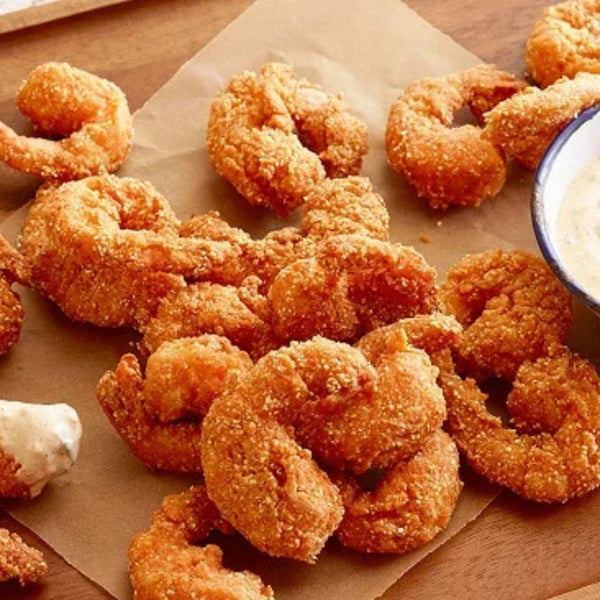 Shrimp Golden offers golden, crispy shrimp arranged on parchment paper with a bowl of creamy dipping sauce, served atop a wooden surface—the perfect seafood snack.