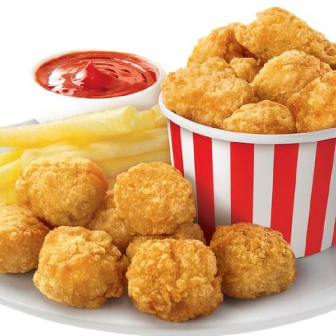 A plate of Chicken Bites with crispy French fries and a red-and-white striped bucket of nuggets. A small cup of ketchup sits next to the fries.