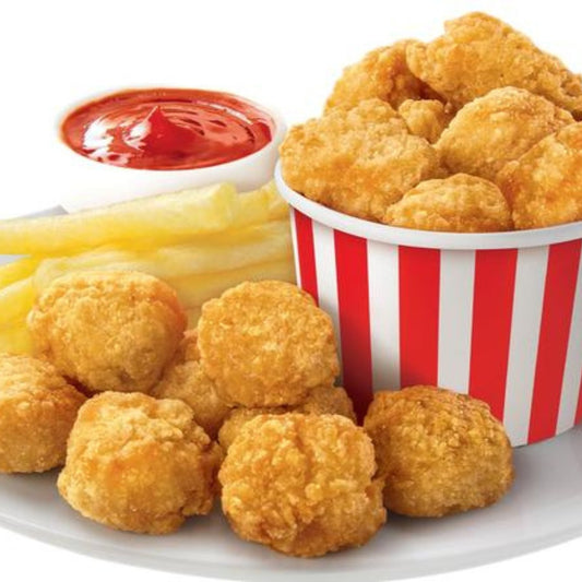 A plate of Chicken Bites with crispy French fries and a red-and-white striped bucket of nuggets. A small cup of ketchup sits next to the fries.