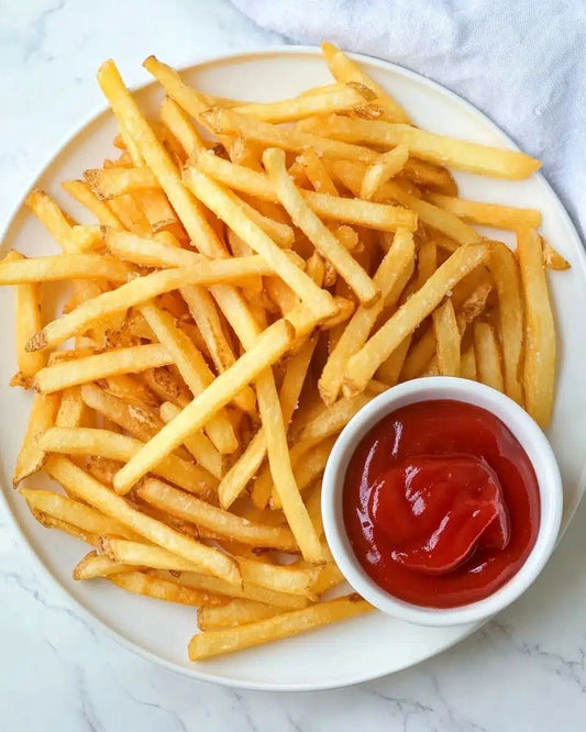 Mac Fries, made from premium potatoes, are served golden and crispy with a side of ketchup in a small white bowl on a light surface.